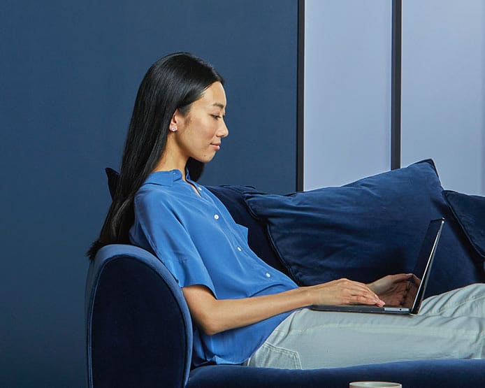 Woman sitting on a blue couch, using a laptop to research mortgage options and understand credit reports.