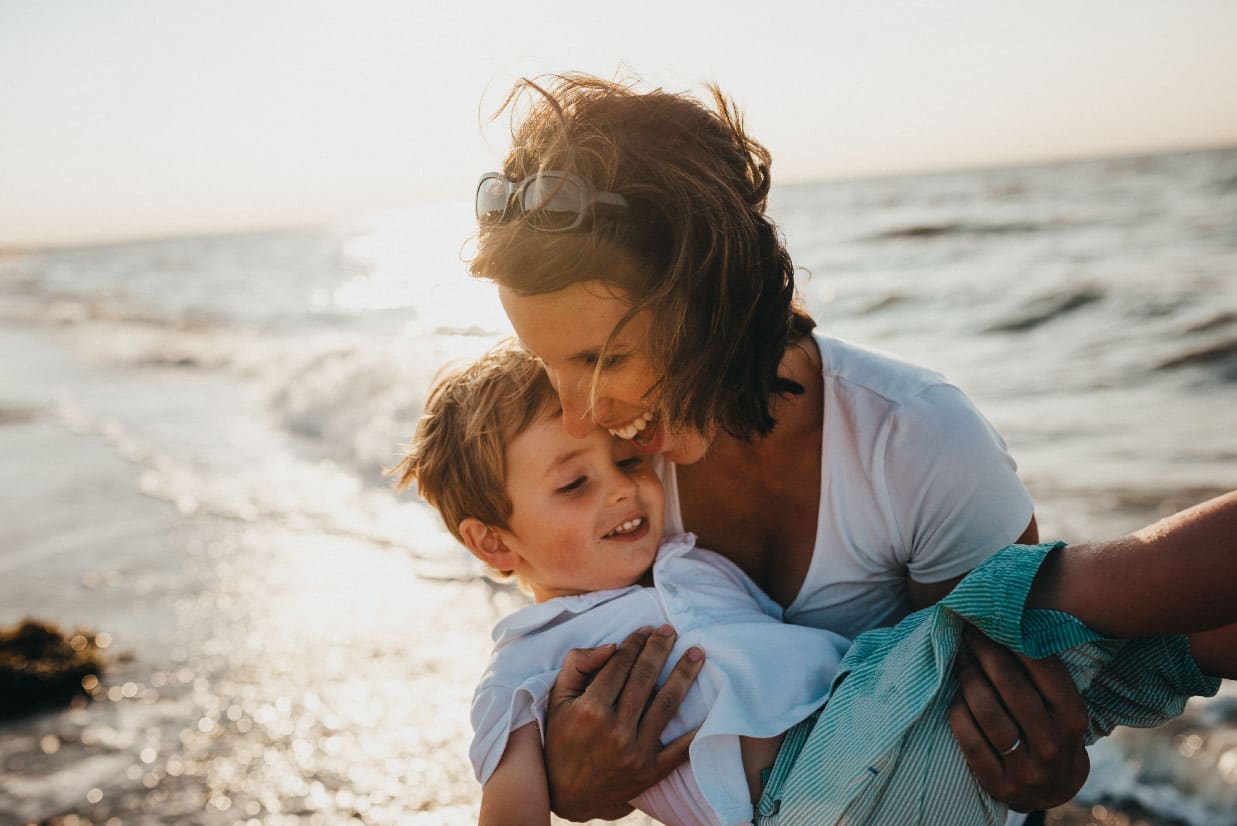 Mother joyfully holding her son at the beach, illustrating family moments and the importance of financial planning for future stability.