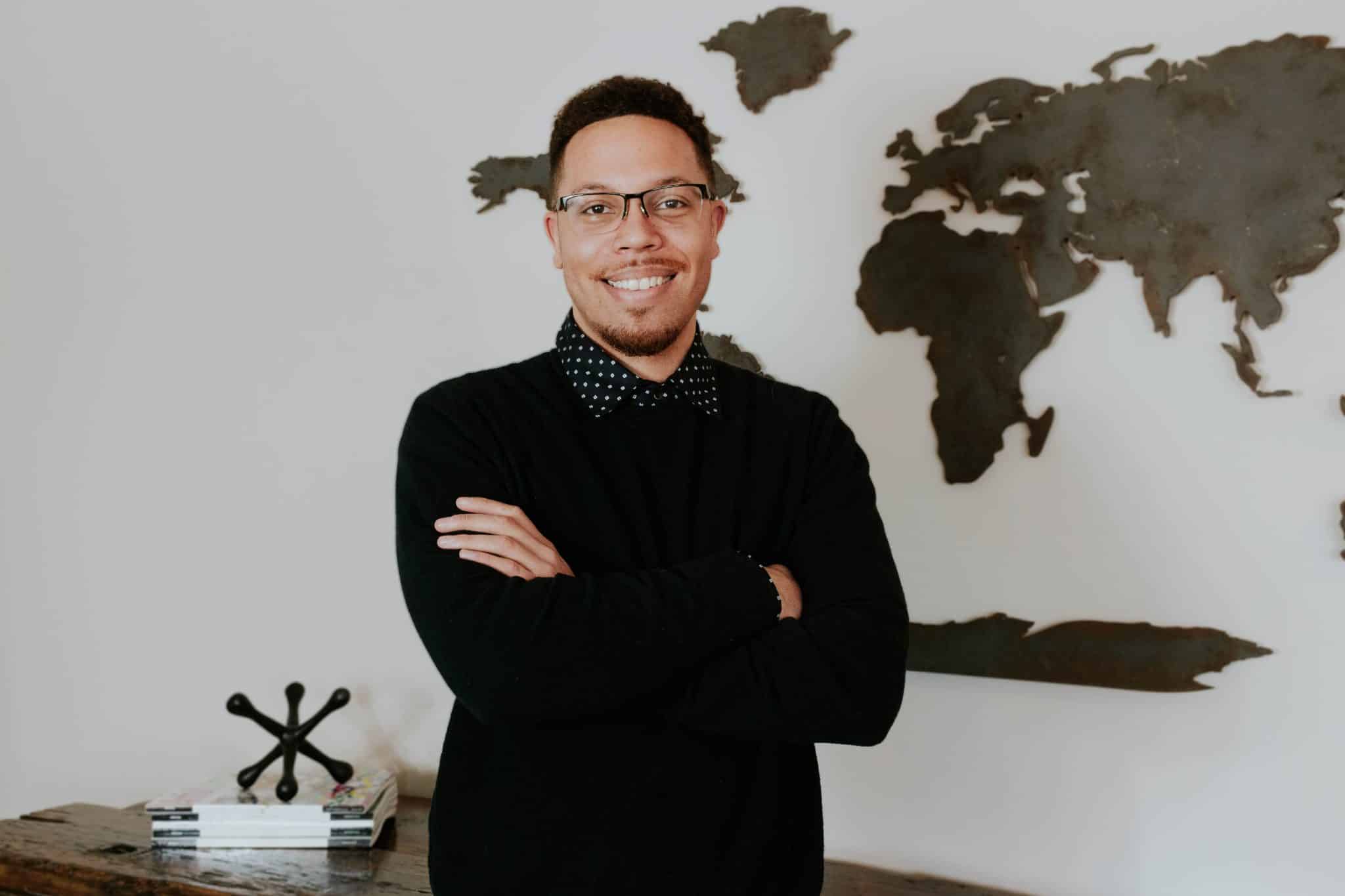 Andrew Mitchell, Mortgage Loan Originator at Refined Lending, smiling with arms crossed in front of a world map backdrop, showcasing a professional and approachable demeanor.