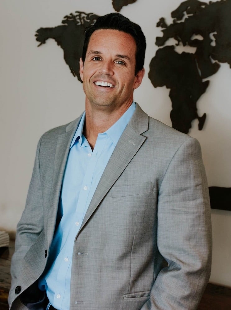 John Miller, Mortgage Loan Originator at Refined Lending, smiling in a professional gray suit against a world map backdrop.