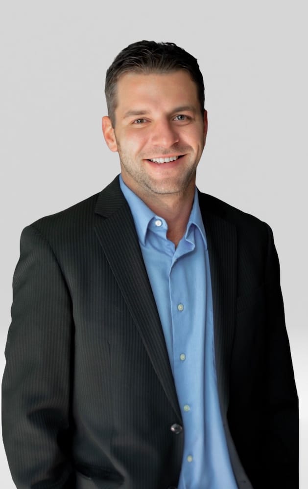 Smiling man in a black suit and light blue shirt, representing professionalism and approachability in a business context.