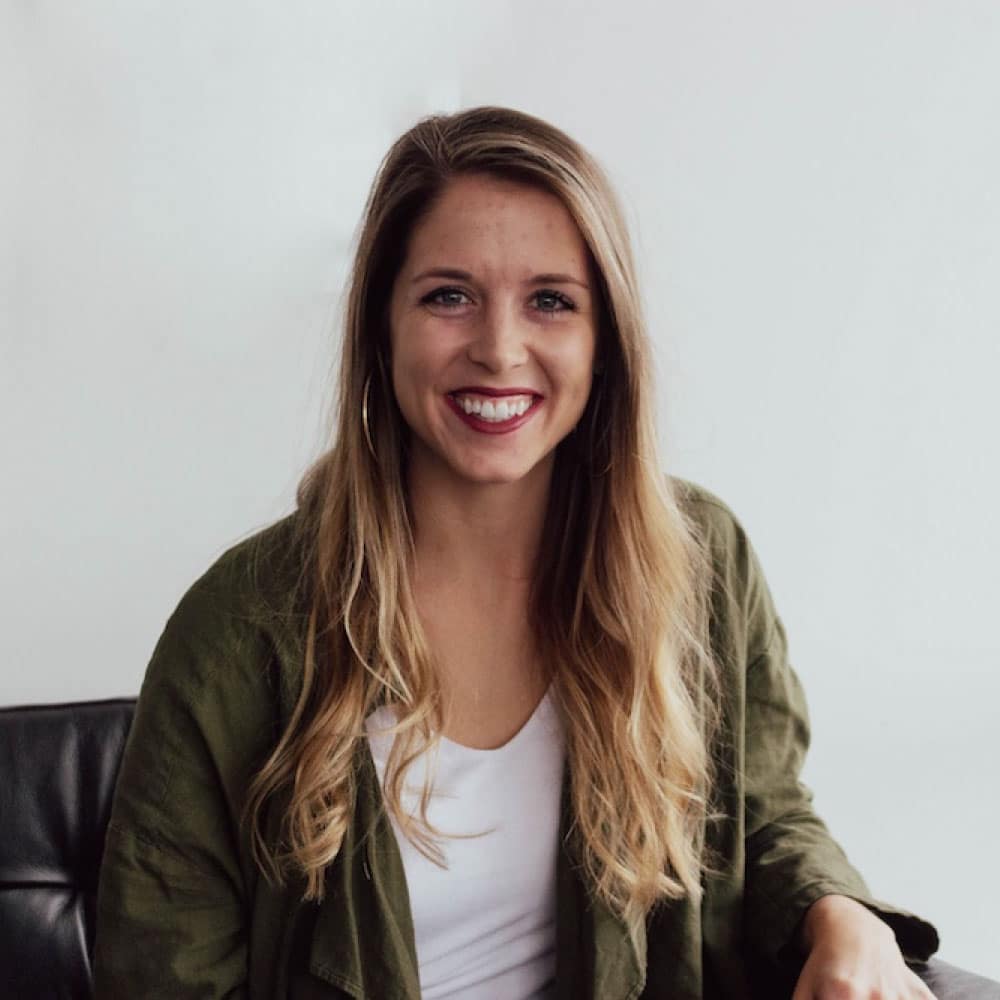 Smiling woman with long hair wearing a green jacket, seated against a light background, representing a friendly and approachable atmosphere in a lending context.