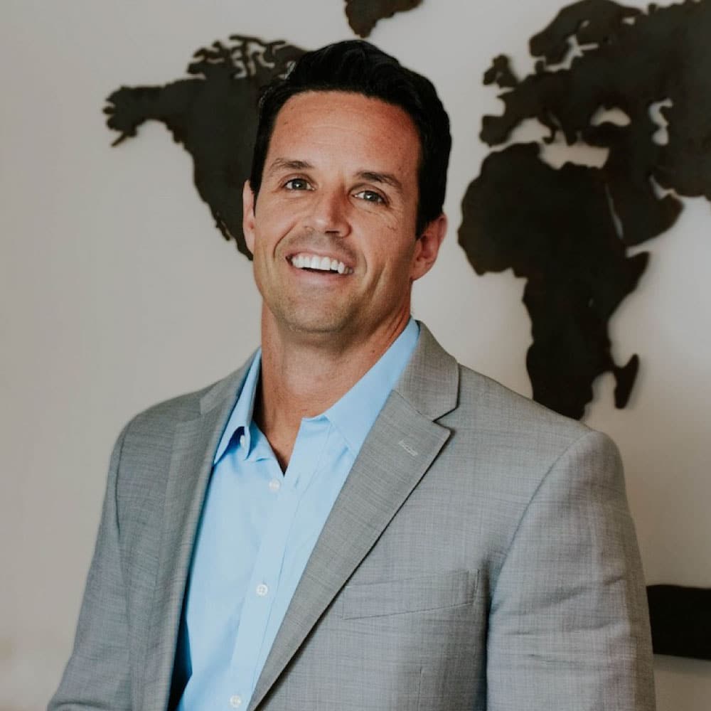 John Miller, Mortgage Loan Originator at Refined Lending, smiling in a professional setting with a world map backdrop.