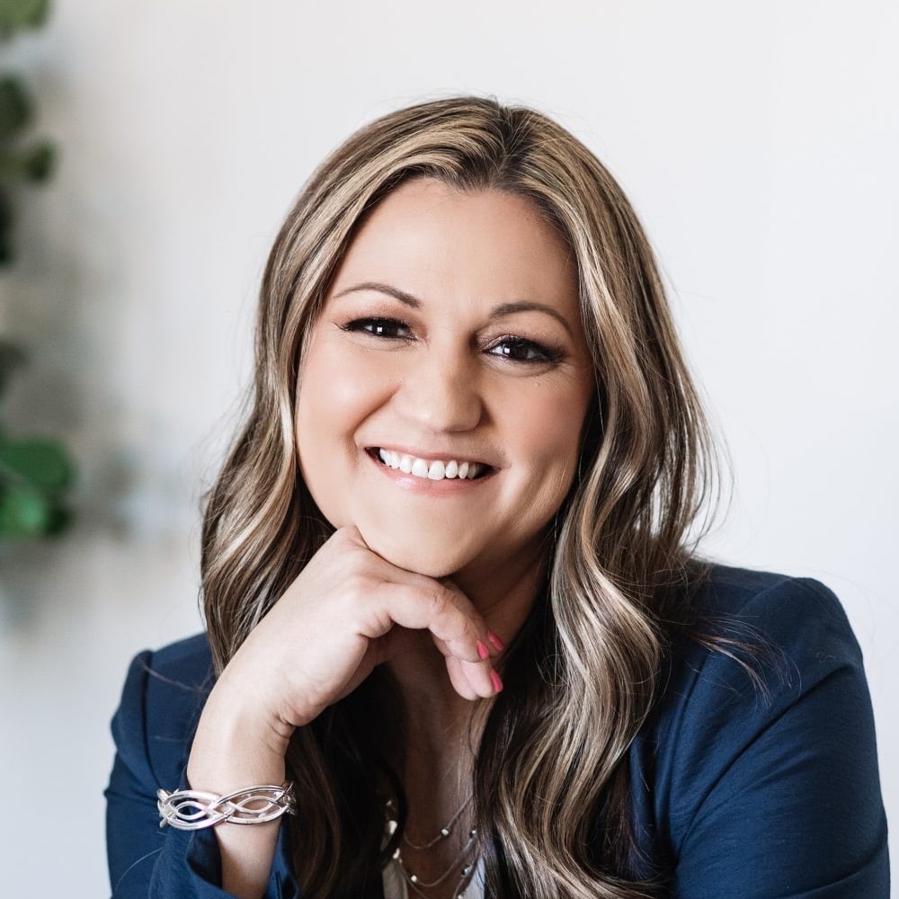 Lindsey Buchanan, smiling mortgage loan originator at Refined Lending, with long hair and a professional blue blazer, showcasing approachable demeanor.