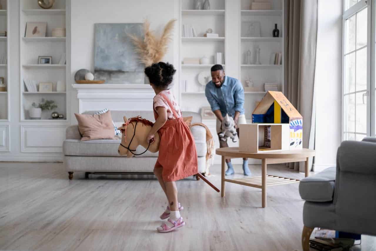 Child playing with a toy horse in a bright living room, while an adult engages with a plush toy, emphasizing family interaction and home life.